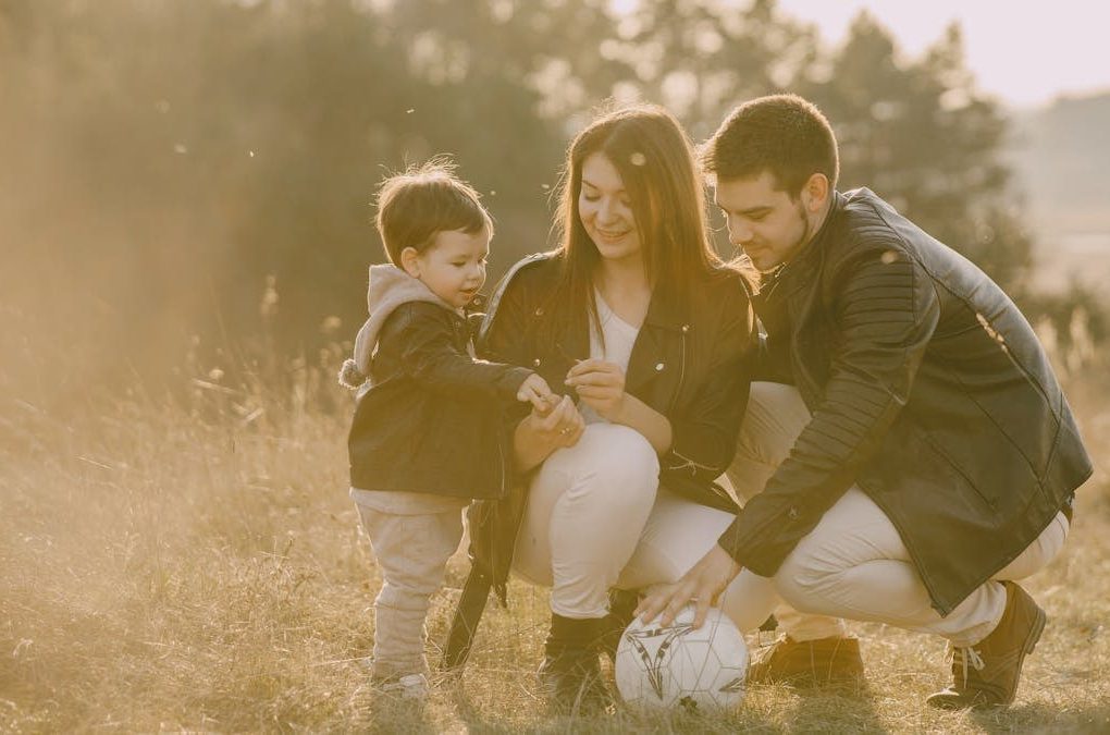A cheerful family bonding outdoors with a soccer ball, enjoying a sunny day in the grass.