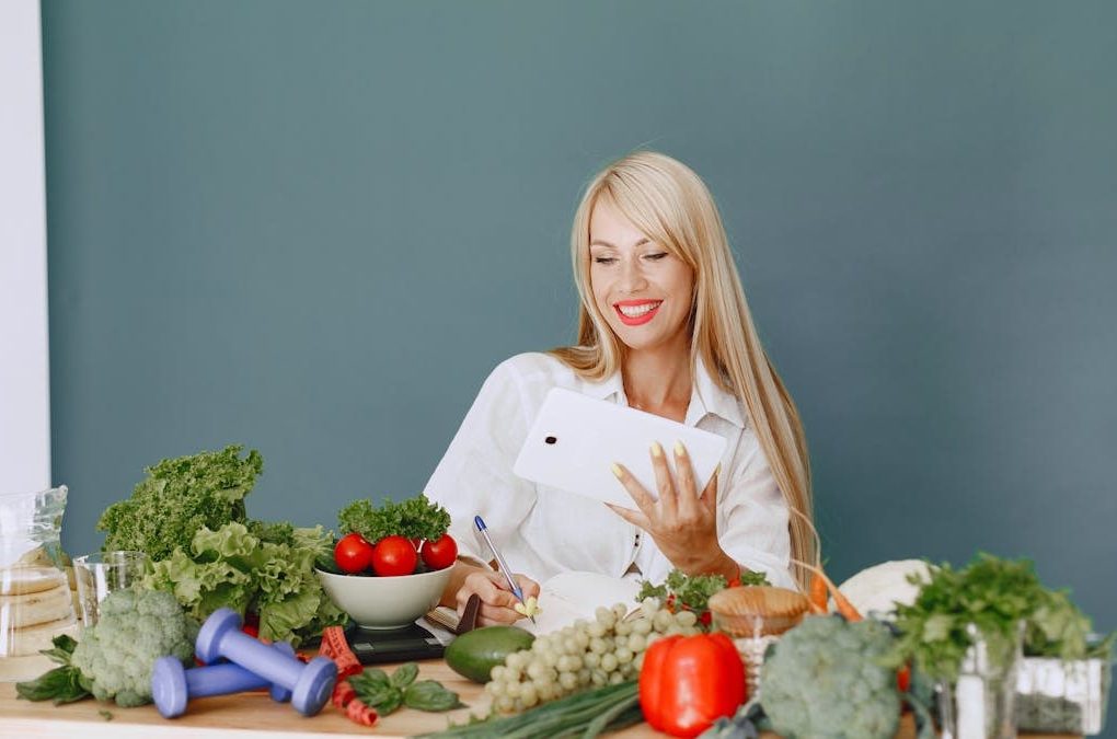 Woman using a tablet surrounded by fresh vegetables at a table, showcasing healthy lifestyle and technology.