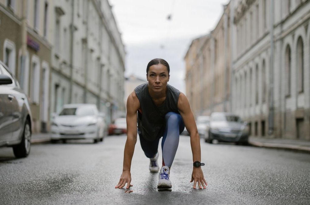 Woman in activewear poised for a run on a city street, symbolizing fitness and determination.